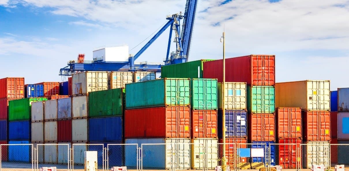 Stacked shipping containers in a terminal yard beneath a blue quay crane.